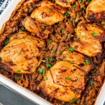 Baked chicken thighs and rice casserole in a white dish with golden, seasoned chicken pieces on top and parsley garnish.
