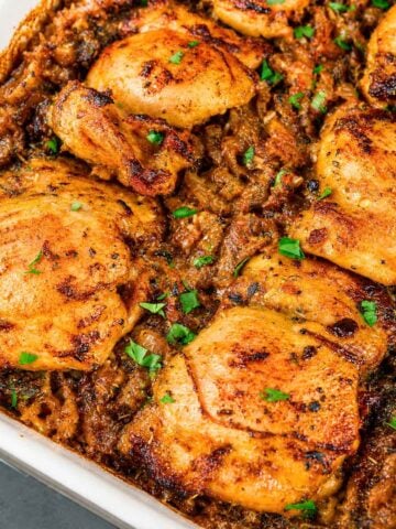 Baked chicken thighs and rice casserole in a white dish with golden, seasoned chicken pieces on top and parsley garnish.