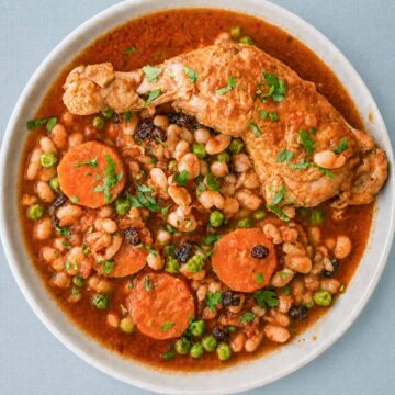 Chicken stew with white beans, carrots, peas, and raisins in a rich tomato sauce, served with fresh parsley on top.