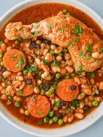 Chicken stew with white beans, carrots, peas, and raisins in a rich tomato sauce, served with fresh parsley on top.