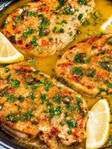 Lemon Chicken Piccata with golden chicken breasts simmered in a tangy lemon butter sauce with capers, garnished with fresh parsley and lemon slices.