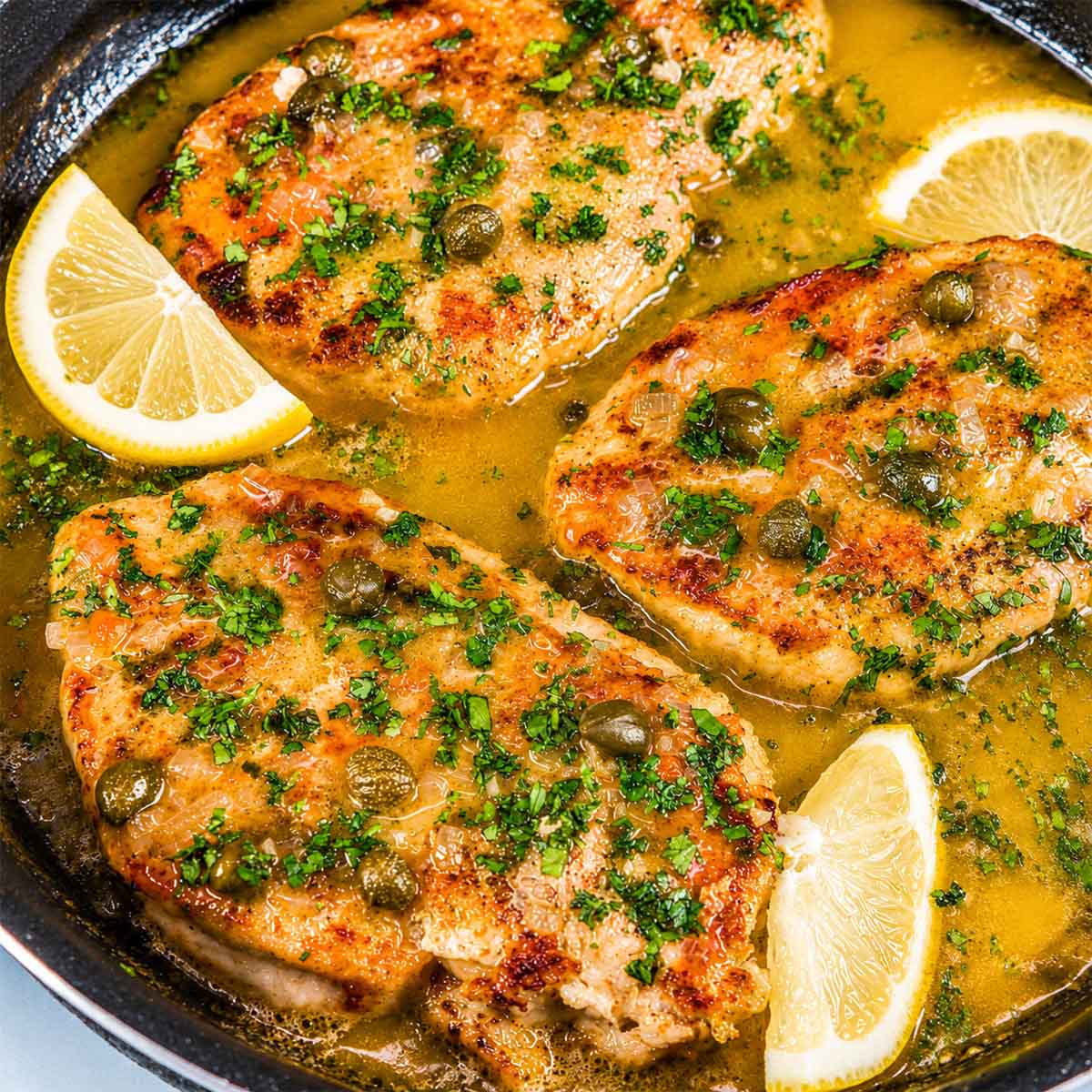 Lemon Chicken Piccata with golden chicken breasts simmered in a tangy lemon butter sauce with capers, garnished with fresh parsley and lemon slices.
