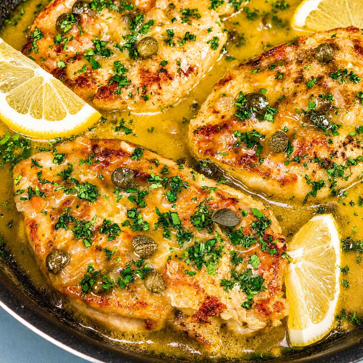 Lemon Chicken Piccata in a skillet with golden seared chicken breasts, capers, fresh parsley, and lemon wedges in a bright buttery sauce.