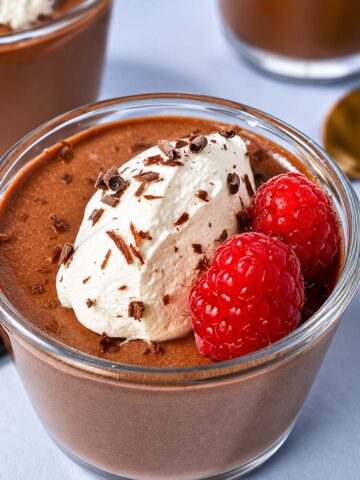 Creamy cottage cheese chocolate mousse topped with whipped cream, fresh raspberries, and chocolate shavings
