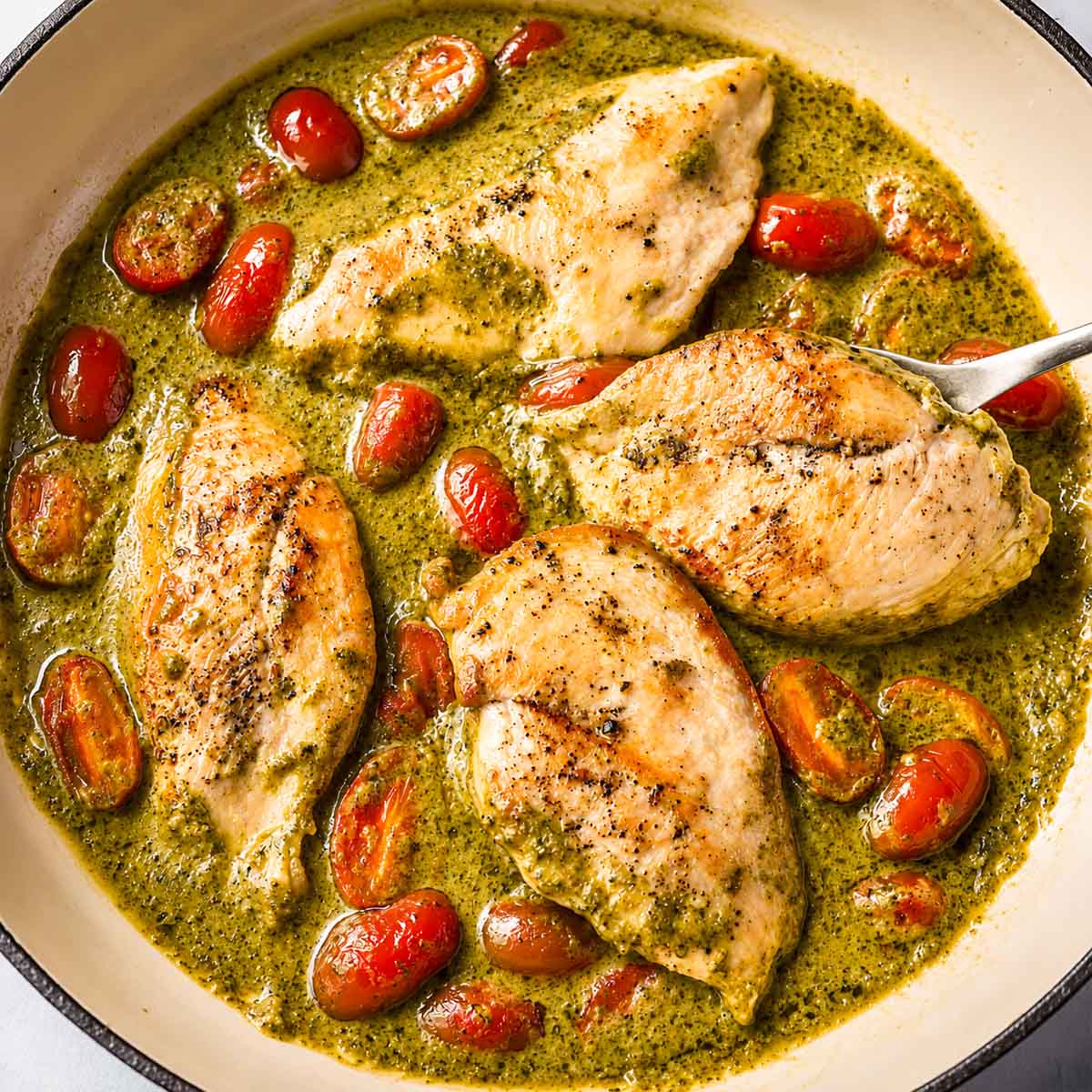 Creamy pesto chicken with cherry tomatoes cooked in a skillet with a rich Parmesan pesto cream sauce