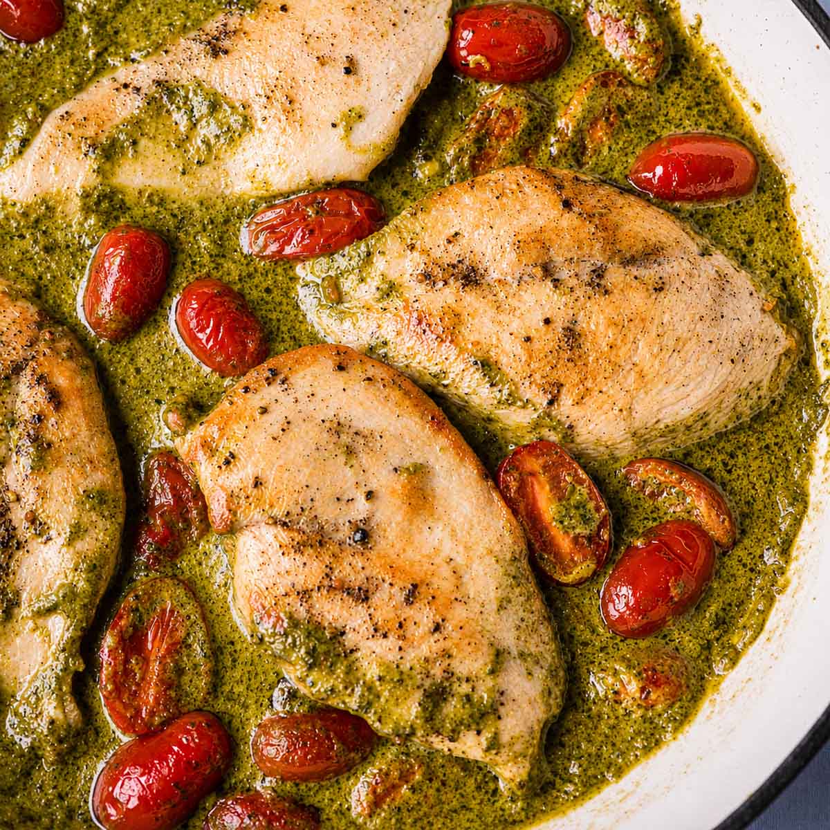 Close-up of creamy pesto chicken in a creamy basil pesto sauce with juicy cherry tomatoes in a skillet