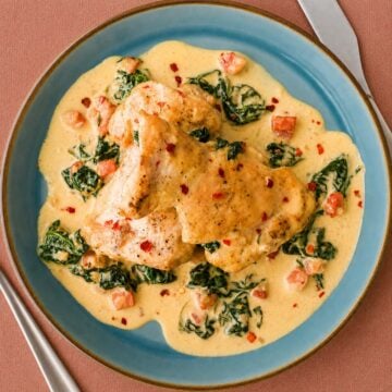 Creamy spinach chicken thighs served in a rich garlic cream sauce with bacon and spinach on a blue plate.