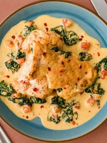 Creamy spinach chicken thighs served in a rich garlic cream sauce with bacon and spinach on a blue plate.