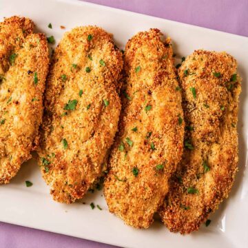 Crispy baked Parmesan crusted chicken on a white platter with a golden panko and Parmesan coating, garnished with fresh parsley.