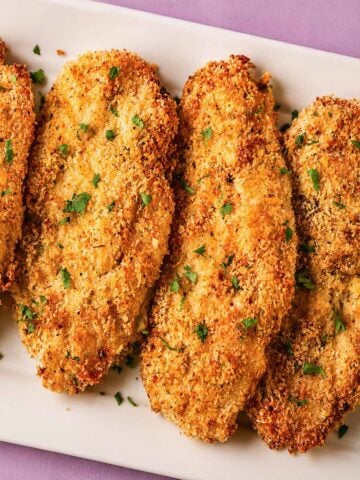 Crispy baked Parmesan crusted chicken on a white platter with a golden panko and Parmesan coating, garnished with fresh parsley.