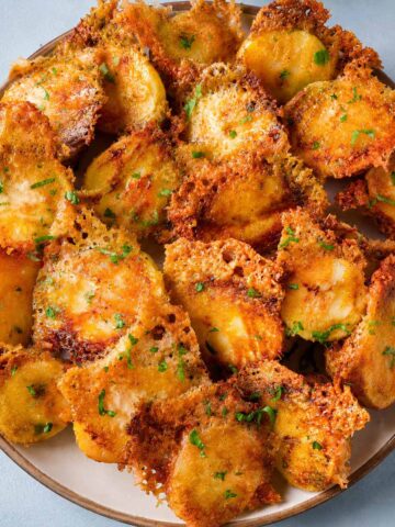 Crispy Parmesan Potatoes with Golden Cheese Crust served on a plate with crispy lacy Parmesan edges and fresh parsley