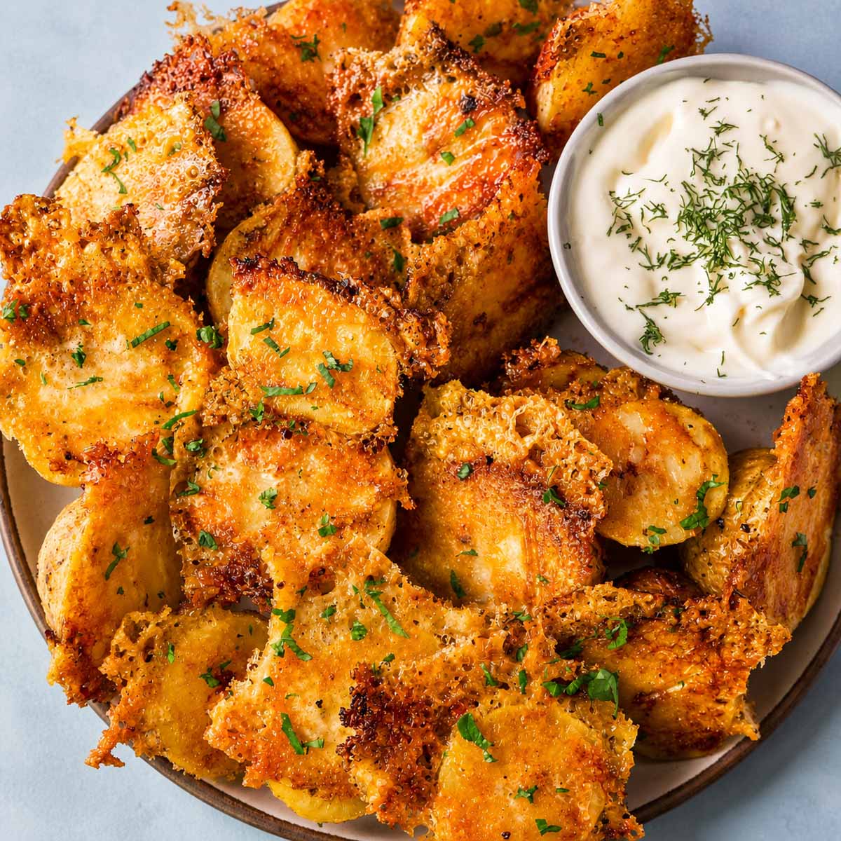 Crispy Parmesan Potatoes with Golden Cheese Crust served with a creamy herb dipping sauce on a ceramic plate