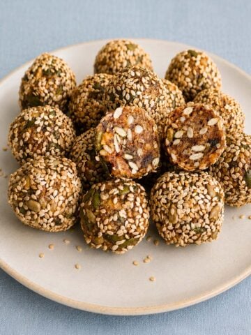 Date balls with walnuts and sunflower seeds coated in sesame seeds, with one ball cut open to show the nutty center