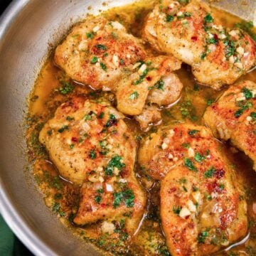 Garlic butter chicken thighs simmering in a skillet with shallots, garlic, parsley, and chili flakes.