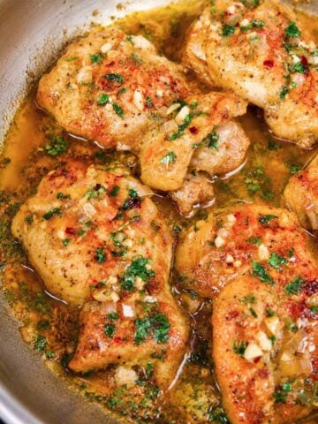 Garlic butter chicken thighs simmering in a skillet with shallots, garlic, parsley, and chili flakes.