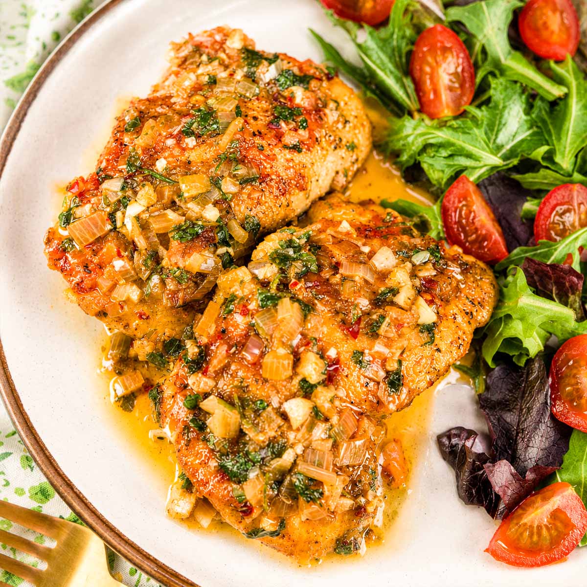 Garlic butter chicken thighs served on a plate with a fresh green salad and cherry tomatoes.