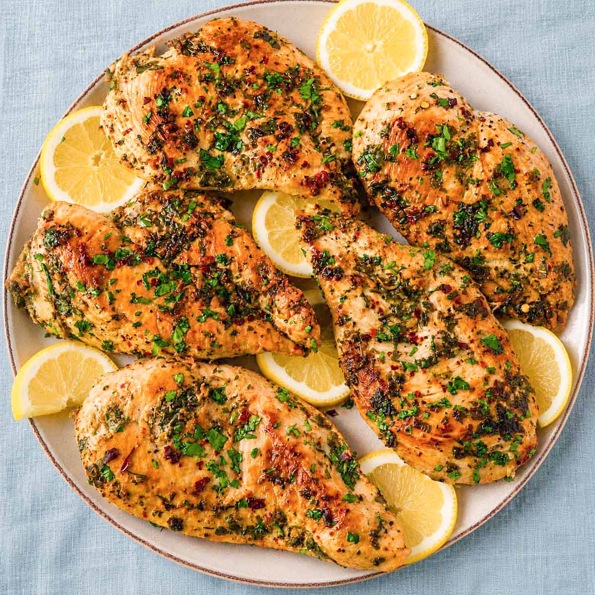Greek lemon chicken cutlets in a skillet topped with chopped parsley and lemon slices.