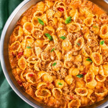 Ground turkey pasta shells in a creamy tomato sauce in a skillet, topped with grated Parmesan and fresh basil leaves.