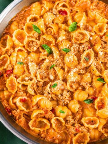 Ground turkey pasta shells in a creamy tomato sauce in a skillet, topped with grated Parmesan and fresh basil leaves.