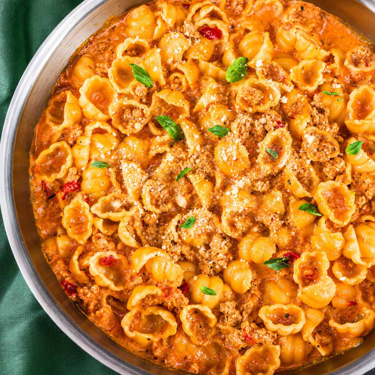 Ground turkey pasta shells in a creamy tomato sauce in a skillet, topped with grated Parmesan and fresh basil leaves.
