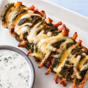Close-up of cheesy Hasselback zucchini stuffed with bacon and served with creamy dipping sauce