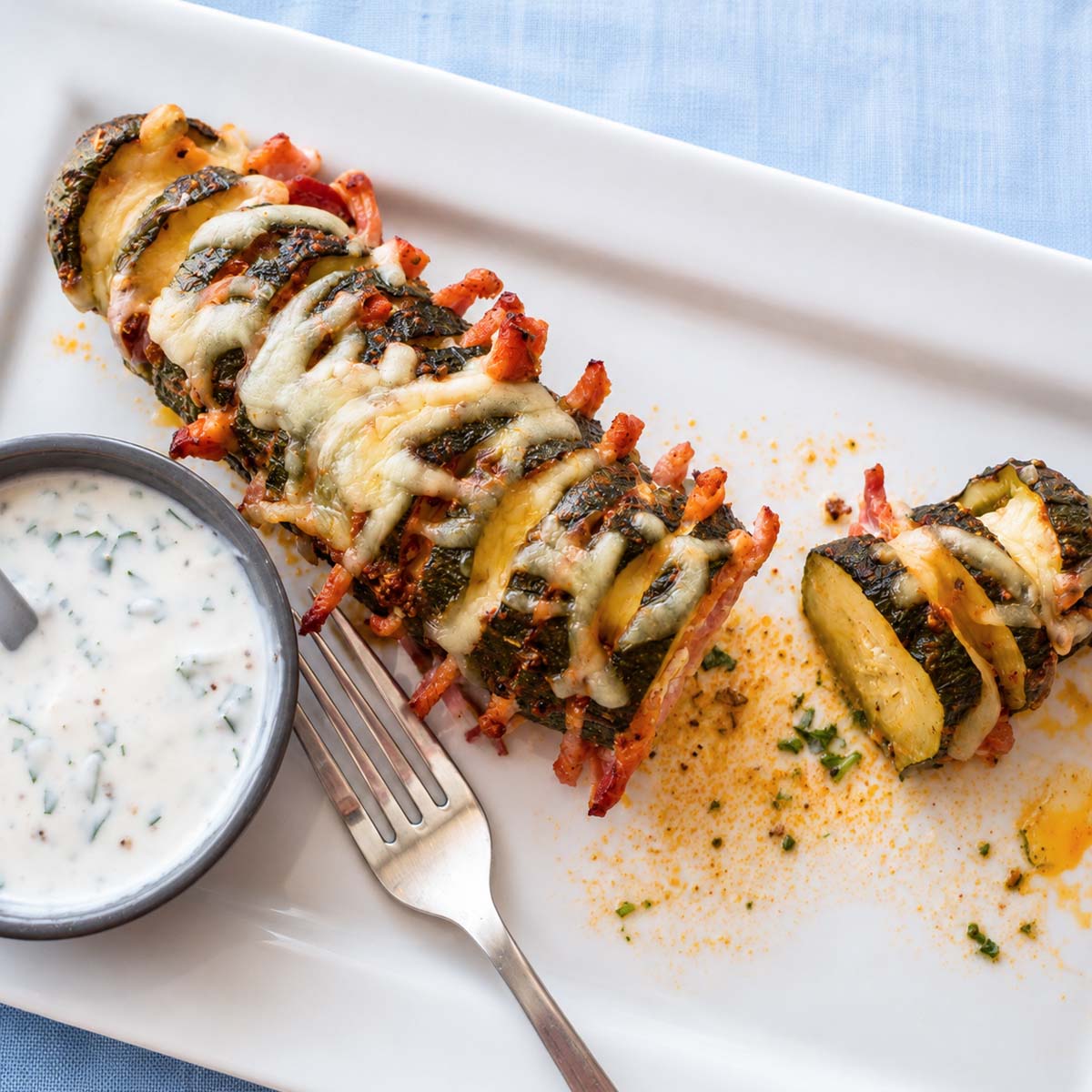 Cheesy baked Hasselback zucchini with bacon, golden roasted edges, and herb sauce