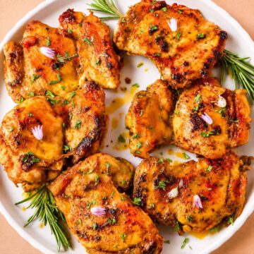 Italian chicken thighs with garlic and lemon, seared golden and served on a white plate with fresh herbs.
