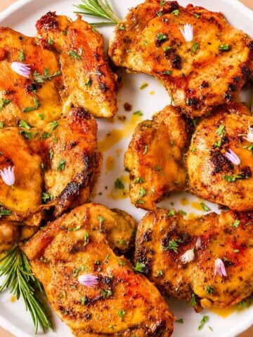 Italian chicken thighs with garlic and lemon, seared golden and served on a white plate with fresh herbs.