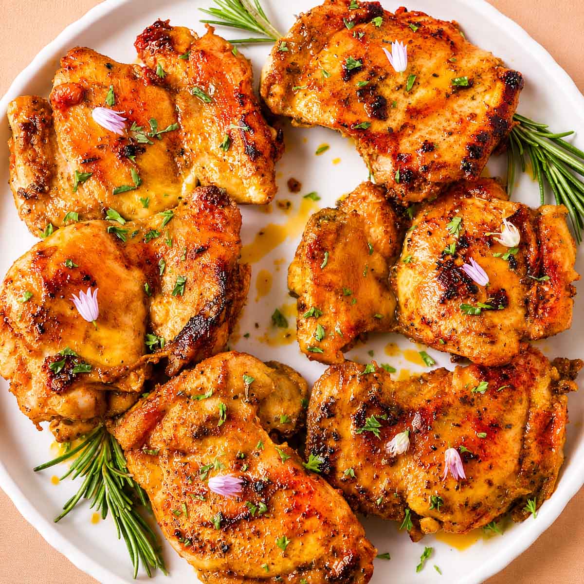 Italian chicken thighs with garlic and lemon, seared golden and served on a white plate with fresh herbs. 