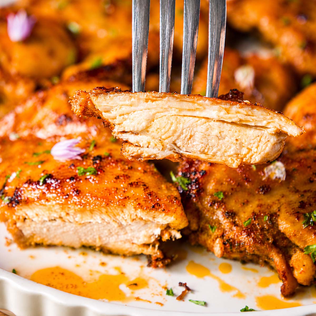 Close-up of Italian chicken thigh with garlic and lemon, a juicy slice held on a fork to show the tender inside.