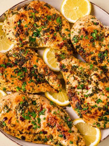 Lemon garlic chicken breasts topped with chopped parsley, served with lemon slices on a white plate.