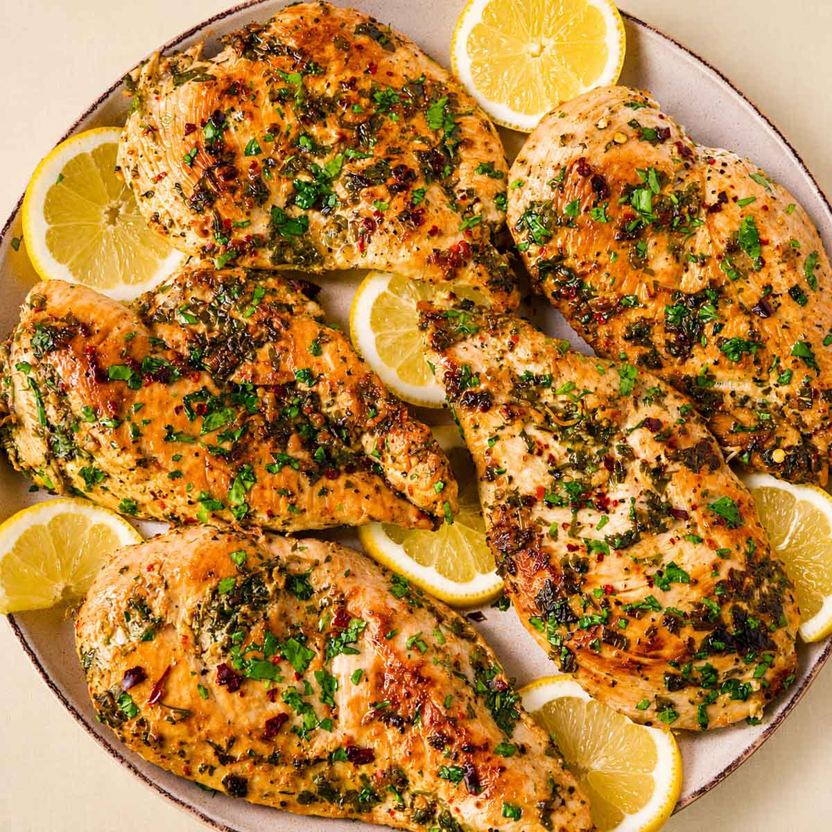 Lemon garlic chicken breasts topped with chopped parsley, served with lemon slices on a white plate.