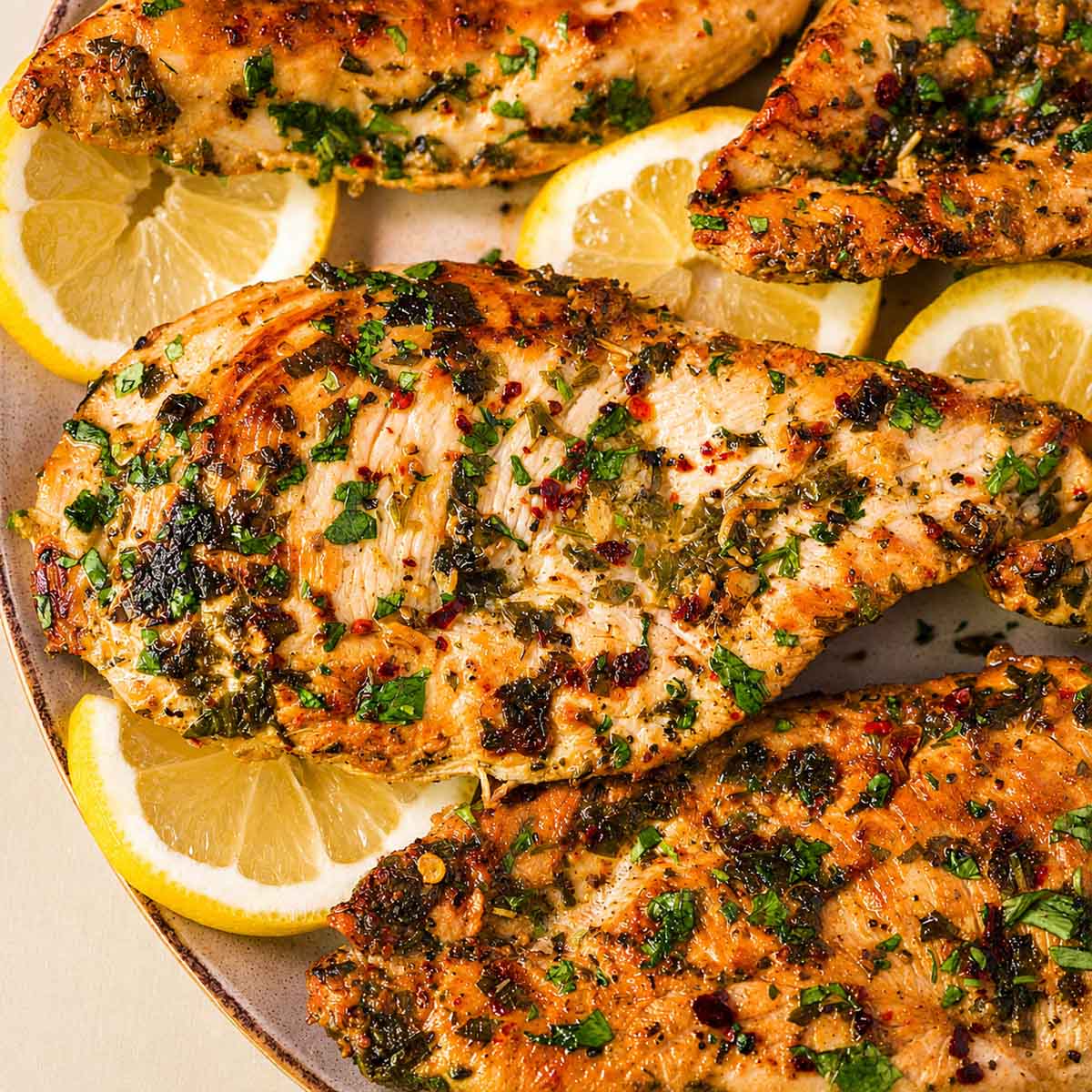 Close-up of lemon garlic chicken breast sprinkled with chopped parsley, with lemon slices tucked underneath.