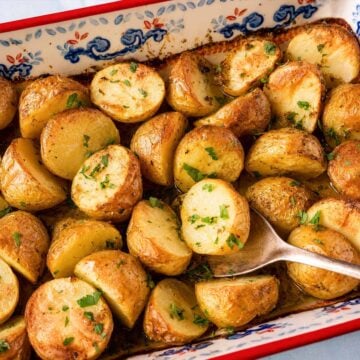 Greek lemon roasted baby potatoes in a ceramic baking dish with garlic, oregano, olive oil, and fresh parsley, roasted until golden and tender.