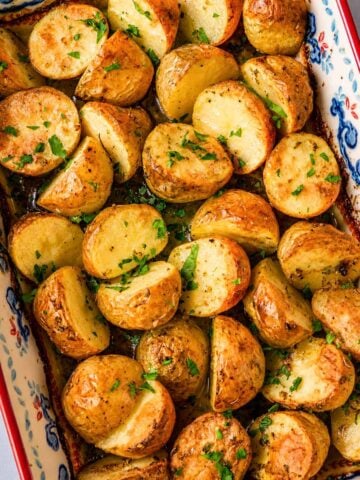 Close-up of Greek lemon roasted baby potatoes with crispy golden edges, garlic, oregano, and fresh parsley in a baking dish.
