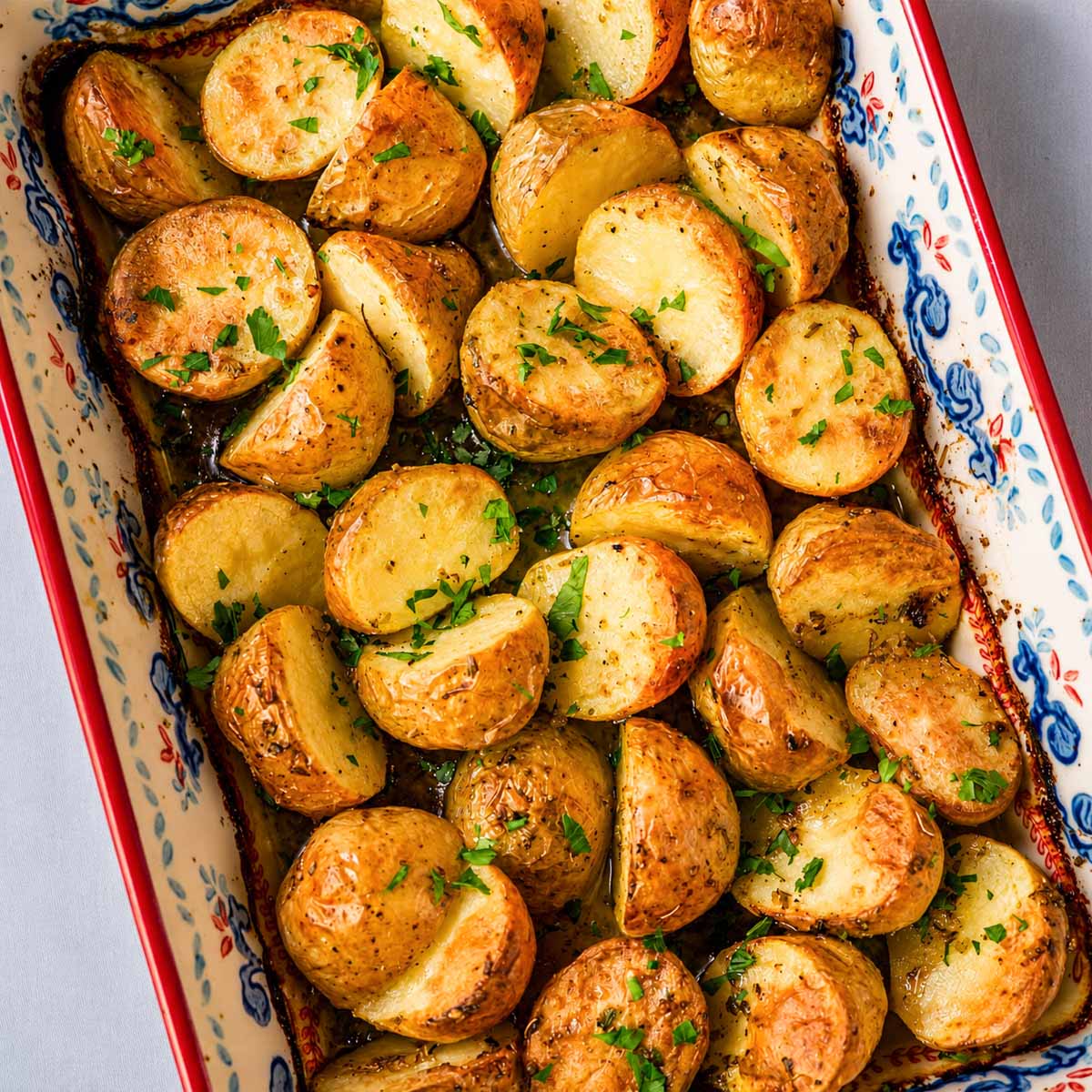 Close-up of Greek lemon roasted baby potatoes with crispy golden edges, garlic, oregano, and fresh parsley in a baking dish.