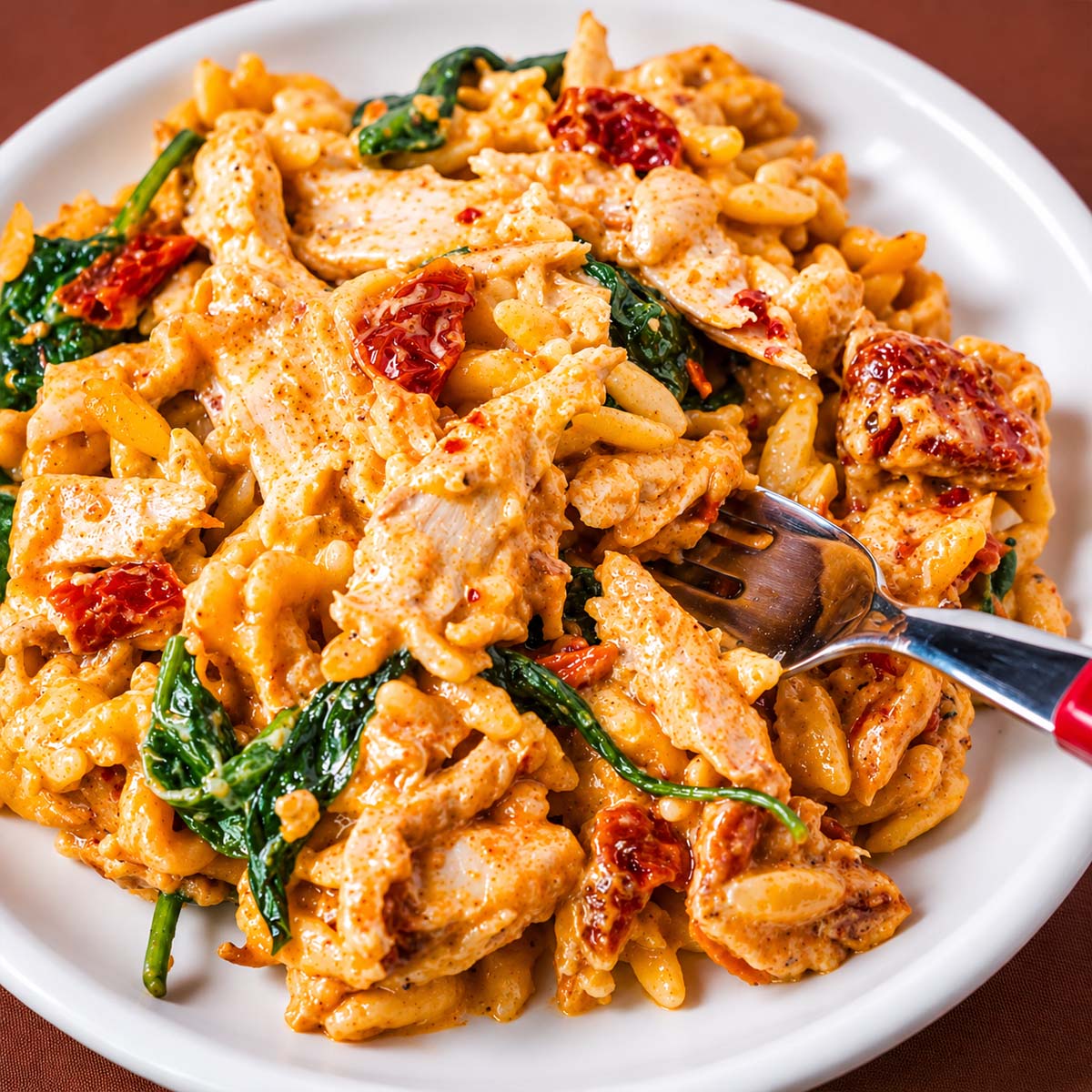 Marry Me chicken orzo served on a white plate with spinach and sun-dried tomatoes