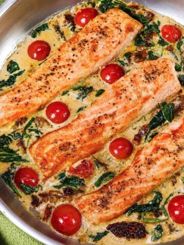 Marry Me Salmon fillets in a creamy sun-dried tomato Parmesan sauce with cherry tomatoes and spinach in a skillet.