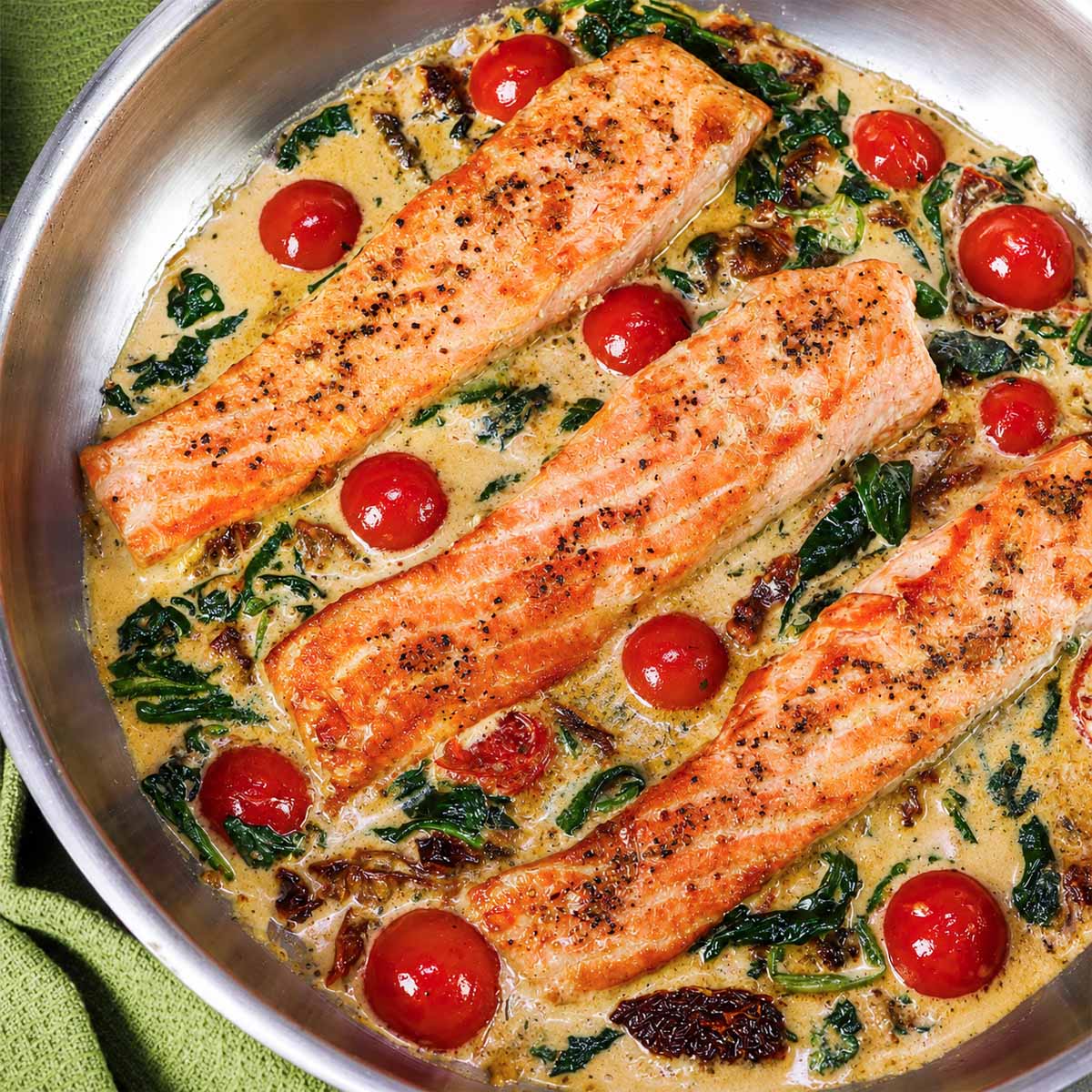 Marry Me Salmon fillets in a creamy sun-dried tomato Parmesan sauce with cherry tomatoes and spinach in a skillet.
