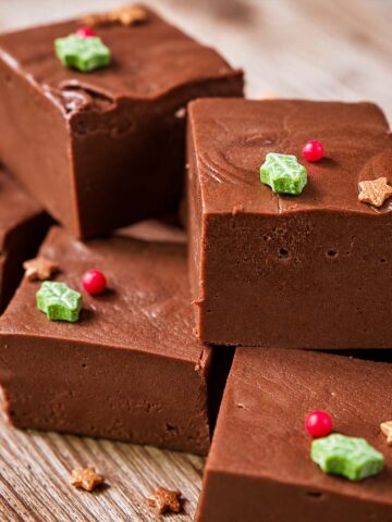 Rich chocolate marshmallow fudge squares topped with festive holiday sprinkles on a wooden plate.