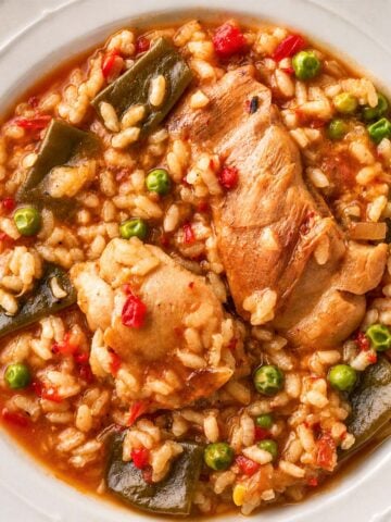 One pot Spanish chicken and rice with tender chicken pieces, peas, and green beans in a rich tomato-based sauce, served in a white bowl.
