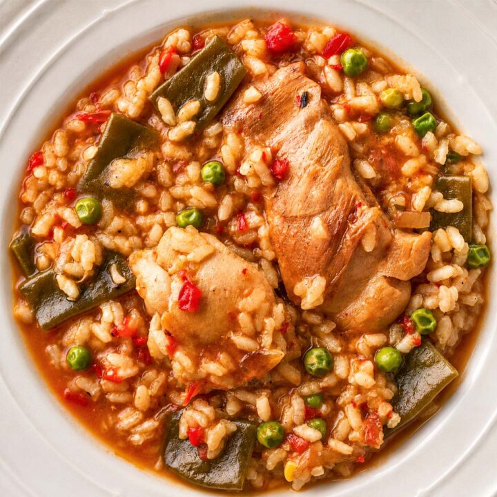 One pot Spanish chicken and rice with tender chicken pieces, peas, and green beans in a rich tomato-based sauce, served in a white bowl.
