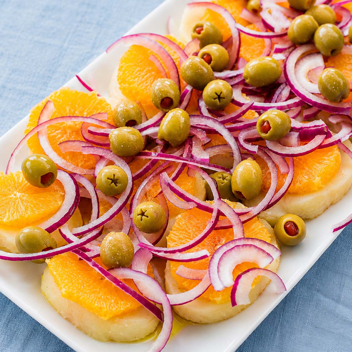 Spanish potato salad with orange slices, green olives, and thinly sliced red onion on a white serving platter.