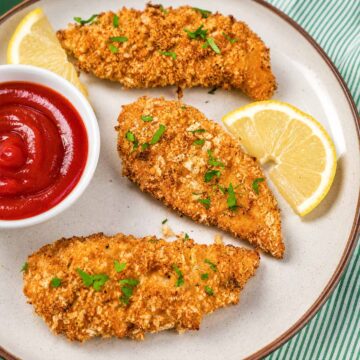 Oven baked chicken tenders with crispy panko coating, ketchup, lemon wedges, and parsley