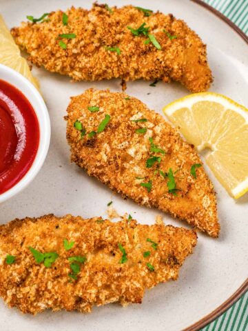 Oven baked chicken tenders with crispy panko coating, ketchup, lemon wedges, and parsley