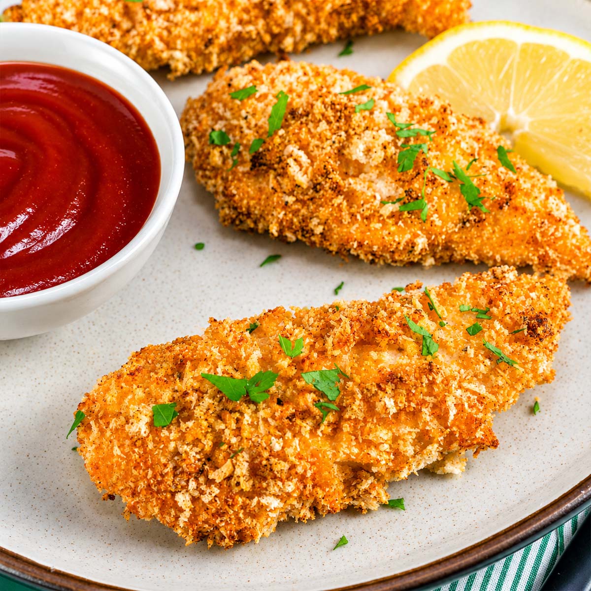 Close-up of crispy oven baked chicken tenders served with ketchup and fresh lemon