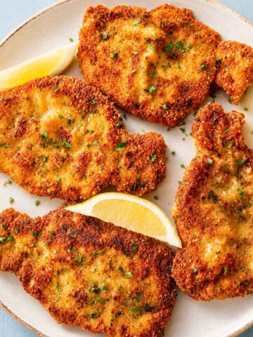 Crispy Pork Milanese served with lemon wedges on a plate, featuring golden breaded pork cutlets with a crunchy Parmesan breadcrumb coating.