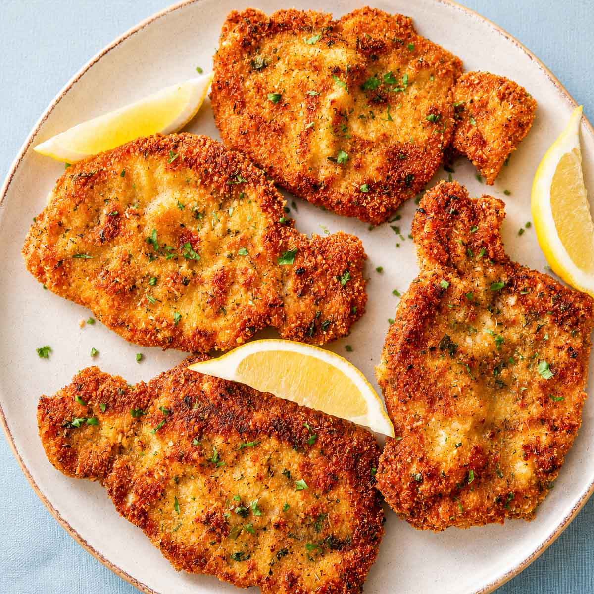 Crispy Pork Milanese served with lemon wedges on a plate, featuring golden breaded pork cutlets with a crunchy Parmesan breadcrumb coating.