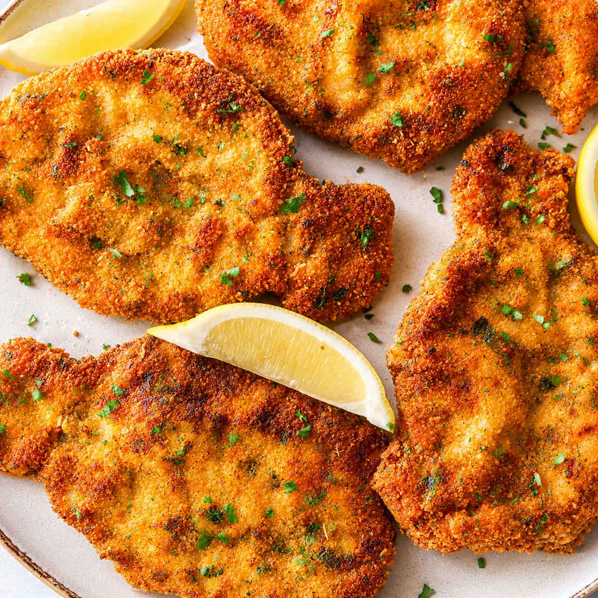 Crispy breaded Pork Milanese served with fresh arugula and a lemon wedge on a ceramic plate.