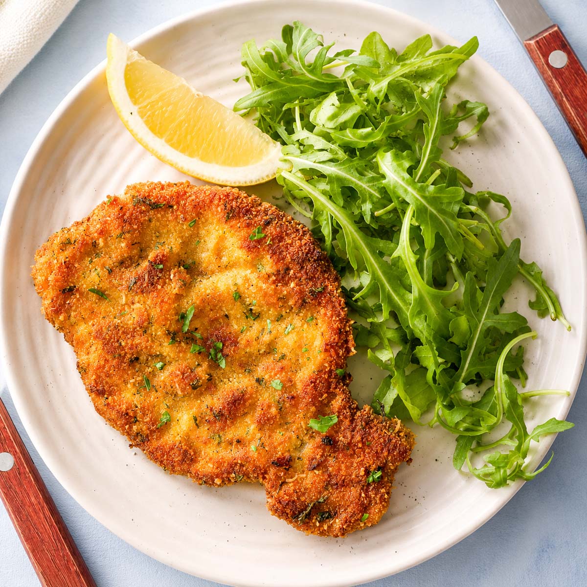 Golden crispy Pork Milanese breaded pork cutlets arranged on a serving platter with lemon wedges and fresh salad leaves.